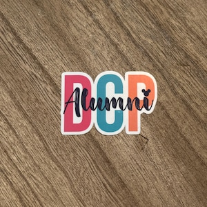 May include: A sticker with the letters "DCP" in pink, teal, and orange, with the word "Alumni" in cursive script. A small Mickey Mouse head is next to the letter "P". The sticker is on a wood grain surface.