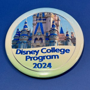 May include: A round button with a light blue, green, and white background. The button features a picture of Cinderella's Castle at Walt Disney World. The text "Disney College Program 2024" is printed in blue on the button.