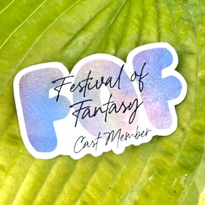 May include: A sticker with a blue, pink, and purple gradient design. The sticker says "Festival of Fantasy" and "Cast Member".