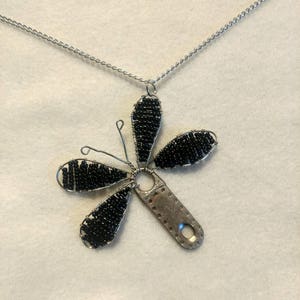 Könnte beinhalten: Eine silberne Kettenkette mit einem schwarzen Perlenblumenanhänger. Die Blume hat fünf Blütenblätter und ein silbernes Mittelstück.