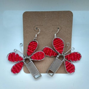 Könnte beinhalten: Ein Paar rote, geperlte Blumenohrringe mit silbernem Draht und einem silbernen Reißverschluss-Zipper. Die Ohrringe hängen an einer braunen Karte.