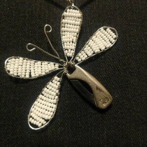 Könnte beinhalten: Eine silberne Halskette mit einem weißen Perlen-Schmetterlingsanhänger. Der Schmetterling hat fünf Flügel und einen silbernen Drahtkörper. Der Anhänger ist an einer silbernen Kette befestigt.