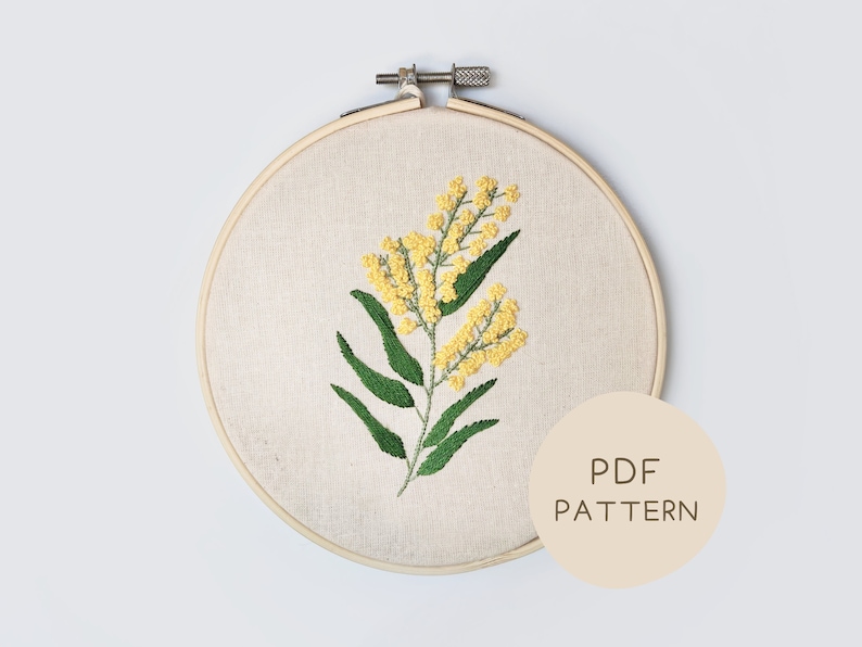 May include: A yellow and green floral embroidery pattern in a wooden embroidery hoop. The hoop is on a white background. The text "PDF PATTERN" is on a beige circle.