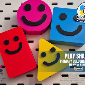 May include: A collection of brightly coloured play shapes in red, pink, blue, and yellow. Each shape has a black smiley face. The image includes the text "PLAY SHAPES PRIMARY COLOURED SHAPES SET OF 4 or 5 SHAPES".