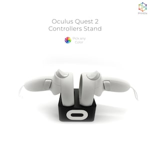 May include: A black stand with a white Oculus logo for holding two white Oculus Quest 2 controllers. The controllers are attached to the stand with their backs facing each other. The stand is on a white background.