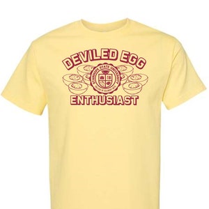 May include: A yellow t-shirt with a red graphic that says "DEVILED EGG ENTHUSIAST" and features a stylized image of deviled eggs and the logo for the "Stanhope State University College of Culinary Arts".