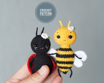 May include: A crocheted ladybug and bee amigurumi toy set. The ladybug is black with red accents and the bee is yellow with black stripes. Both toys have white wings and a white flower on their heads. The toys are held in a hand against a gray background.