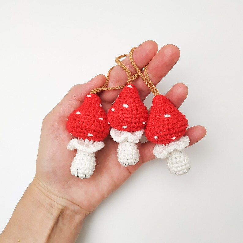 Pu&ograve; includere: Tre ciondoli a forma di fungo in crochet rosso e bianco con steli bianchi e anelli di corda marroni.