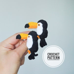 May include: Two handmade crochet toucans. The birds are black with white chests, orange beaks, and small orange feet. The text "CROCHET PATTERN" is in a white circle in the lower right corner.