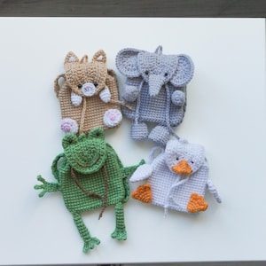 Puede incluir: Cuatro pequeñas mochilas de ganchillo con forma de animales. La colección incluye un gato beige, un elefante gris, una rana verde con extremidades largas y un pato blanco con pico y patas naranjas. Cada bolsa tiene un cierre de cordón.
