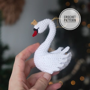 Peut inclure: Ornement de cygne en crochet blanc avec une couronne dorée et un bec rouge. Le cygne tient une ficelle dorée.