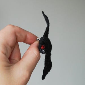 K&ouml;nnte beinhalten: Handgefertigte schwarze H&auml;kel-Fledermaus-Anstecknadel mit roten und wei&szlig;en Akzenten. Die Fledermaus hat einen kleinen roten Mund und wei&szlig;e Z&auml;hne. Ein silberner Verschluss befestigt die Nadel. Einzigartiges Accessoire.