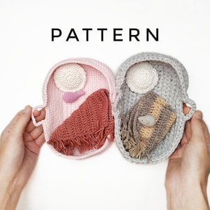 May include: Two crocheted baby baskets, one pink and one gray, each containing a crocheted item. The pink basket holds a white circle, a pink fish, and a red fringed scarf. The gray basket holds a white circle, a striped scarf, and a gray bird. The word "PATTERN" is above the baskets.