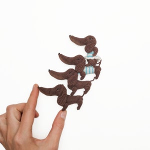 May include: Four brown crocheted dachshund dog figurines lined up in a row, with the smallest one at the front and the largest one at the back.