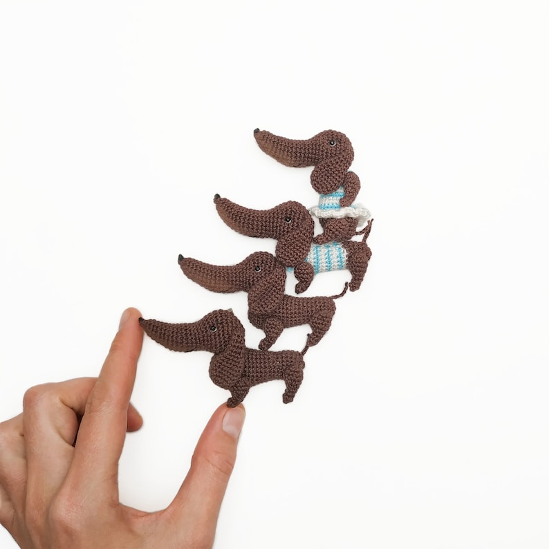 May include: Four brown crocheted dachshund dog figurines lined up in a row, with the smallest one at the front and the largest one at the back.