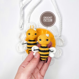Può includere: Due api all'uncinetto con strisce nere e gialle, che si aggrappano a una margherita bianca all'uncinetto con un centro giallo. La margherita è attaccata a un cinturino bianco all'uncinetto. Il testo "CROCHET PATTERN" è su un cerchio marrone.