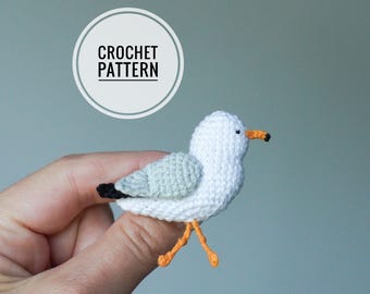 Op de afbeelding: Haakpatroon voor een witte meeuw met oranje poten en een grijze vleugel. De meeuw wordt in een hand gehouden.
