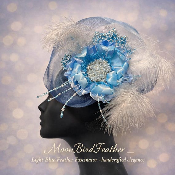 Handcrafted fascinator featuring a sky‑blue satin flower, shimmering beadwork, airy white feathers, and fine mesh details.