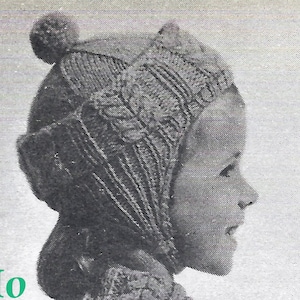 Può includere: Una foto in bianco e nero di un bambino che indossa un cappello di lana con un pon pon in cima. Il cappello ha un design unico con linee verticali e un elemento decorativo sul lato. Il bambino guarda di lato e il cappello gli copre le orecchie.