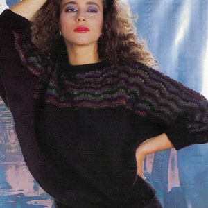 May include: A woman wearing a black sweater with a colorful striped pattern around the neck. The sweater has long sleeves and a loose fit. The woman is wearing a black skirt and has long brown hair. The background is a blue and white abstract design. The text "PDF Pattern" is at the bottom of the image. The text "Io" is at the top of the image.