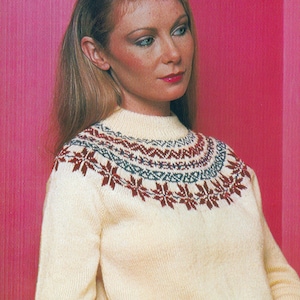 May include: A white knitted jumper with a colourful geometric pattern around the neckline. The jumper is being worn by a woman with long blonde hair. The text "Io" and "PDF Pattern" are visible in the image.