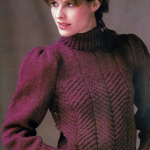 May include: A purple knitted sweater with a high neck and a chevron pattern. The sweater has puffed sleeves and is shown on a model wearing a patterned headband. The text "PDF Pattern" is at the bottom of the image.