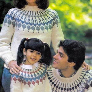Pode incluir: Uma família vestindo suéteres de tricô branco com padrões geométricos coloridos. Os suéteres têm gola redonda e são usados ​​sobre calças jeans azuis. A imagem inclui o texto "PDF Pattern" e "Io".