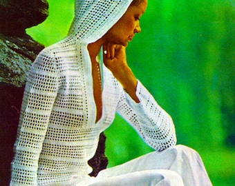 May include: A crochet top with a hood, long sleeves, and a deep V-neck. The top is white and has a lacy pattern. The model is wearing white pants and is sitting on a rock. The image has the text "PDF Pattern" at the bottom.