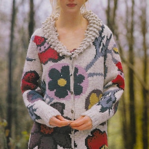 May include: A knitted cardigan with a floral pattern in shades of red, pink, yellow, and blue. The cardigan has a white collar and is buttoned up the front. The text "PDF Pattern" is visible at the bottom of the image.