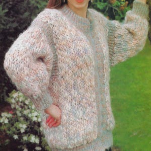 May include: A chunky knit sweater in pastel colors of pink, blue, and beige. The sweater has a crew neck and long sleeves with a ribbed cuff. The overall style is oversized and cozy, perfect for cooler weather. The sweater is made of a thick, textured yarn.