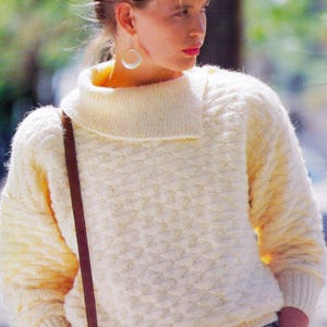 Puede incluir: Un suéter de punto blanco con cuello alto y un patrón de punto de cable. El suéter tiene una correa marrón que va sobre el hombro. El texto "PDF Pattern" está en la parte inferior de la imagen.