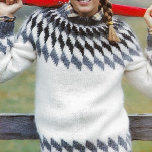 Könnte beinhalten: Ein gestrickter Pullover in Weiß, Grau und Schwarz mit einem Rautenmuster an Passe und Saum. Der langärmlige Pullover ist aus einem weichen, strukturierten Material gefertigt. Ein kariertes Hemd ist darunter zu sehen.
