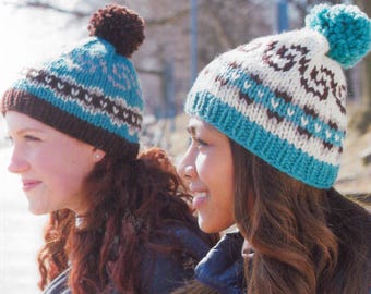 May include: Two knitted winter hats. One hat is brown, teal, and white with a brown pom-pom. The other hat is white, teal, and brown with a teal pom-pom. The hats have a geometric pattern and are worn by two people.