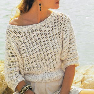 May include: Off-white, open-weave knit top with a boat neck and short sleeves. The top has a ribbed hem and cuffs. The knit pattern creates a textured look. The top is a light, airy garment, suitable for warmer weather.