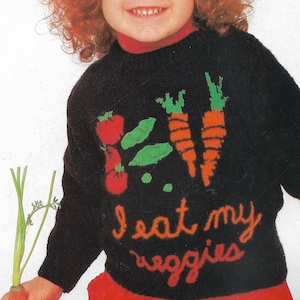 May include: Black sweater with a red turtleneck featuring embroidered vegetables: tomatoes, carrots, and green leaves. The phrase "I eat my veggies" is written in orange script. The sweater is part of a children's clothing collection.