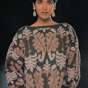 May include: A dark gray sweater with a repeating floral pattern in shades of brown and pink. The sweater has a wide neckline and long sleeves. The model is wearing gold earrings.