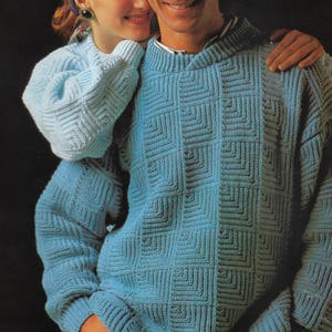 May include: Two light blue knitted sweaters with a geometric square pattern. One sweater has a hood, and the other has a crew neck. The sweaters are made of a soft, textured yarn.
