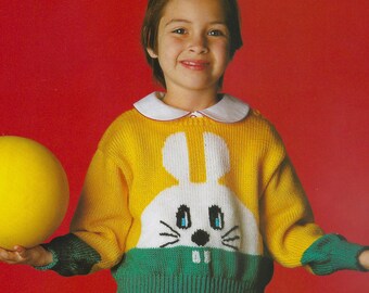 May include: A child wearing a yellow sweater with a white bunny face design. The sweater has a white collar and green cuffs and hem. The background is red.
