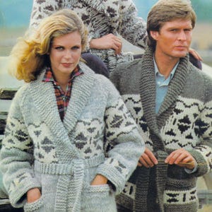 May include: A light grey knitted robe with a shawl collar and a belt, featuring a geometric pattern in white and dark grey. The robe has pockets and is worn over a plaid shirt. The image shows a couple wearing matching robes.
