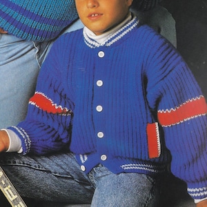Può includere: Un cardigan blu lavorato a maglia con dettagli rossi e bianchi. Il cardigan presenta una trama a coste, bottoni bianchi e un colletto bianco. Strisce rosse adornano le maniche e una tasca rossa è visibile. Abbigliamento per bambini.