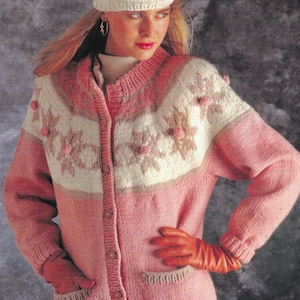May include: A pink knitted cardigan with a white and brown snowflake pattern and pink pom-poms. The cardigan has a button-up front and long sleeves.