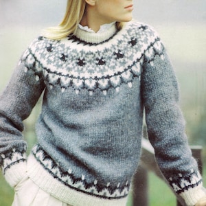 May include: A gray knit sweater with a patterned yoke in white, gray, and black. The sweater has a ribbed collar and cuffs. The model is wearing a white collared shirt underneath. The sweater is a classic, cozy style.