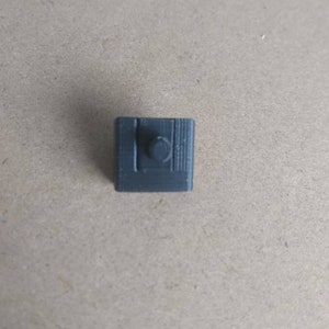 May include: A small, gray, plastic, 3D printed object with a round knob on top.
