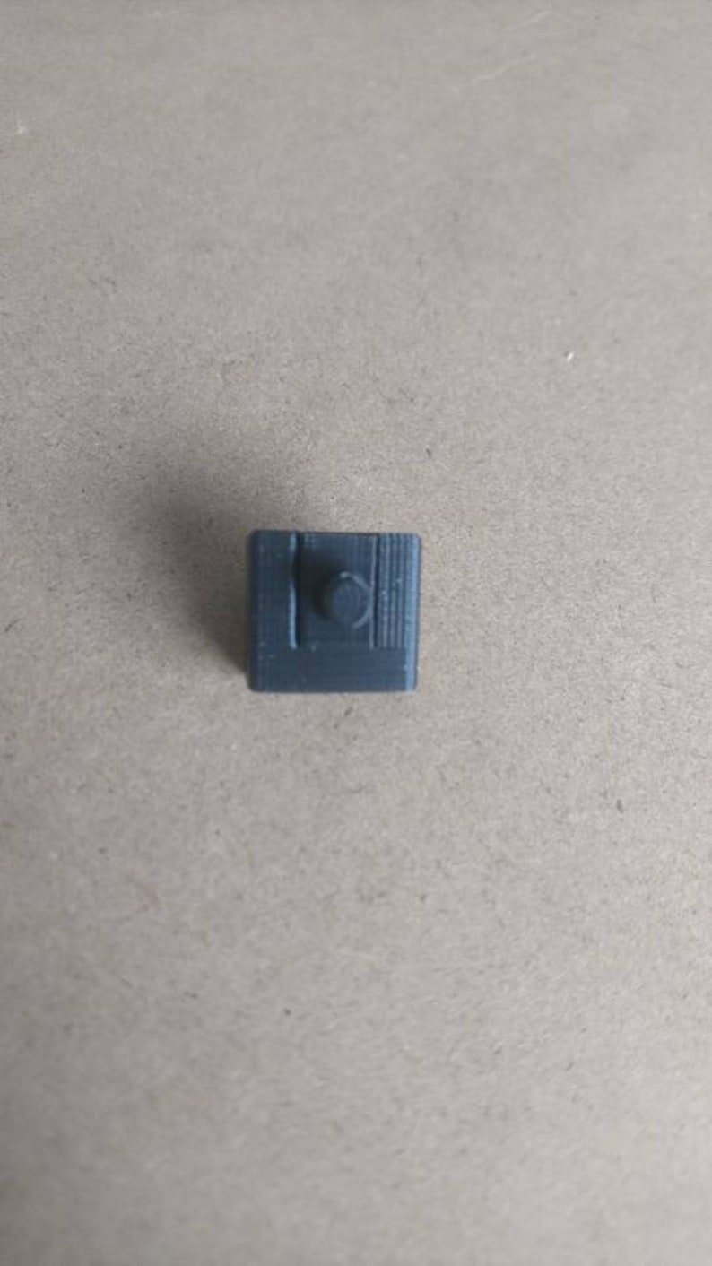 May include: A small, gray, plastic, 3D printed object with a round knob on top.