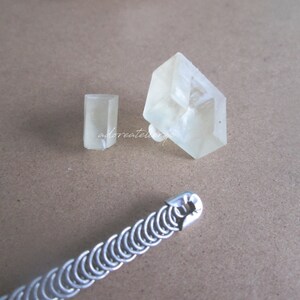 May include: Two clear crystal shapes, one rectangular and one square, on a brown surface. A silver chain link bracelet is also on the surface.