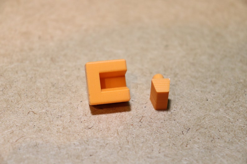 May include: Two orange plastic building blocks, one is a square with a hollow center and the other is a triangular prism.