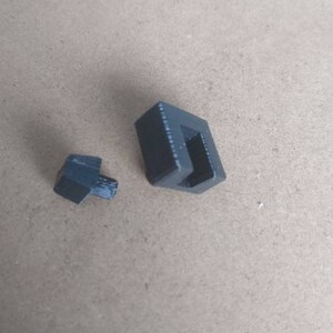 May include: Two black plastic pieces, one is a small square with a hole in the center, the other is a larger rectangular piece with a slot.