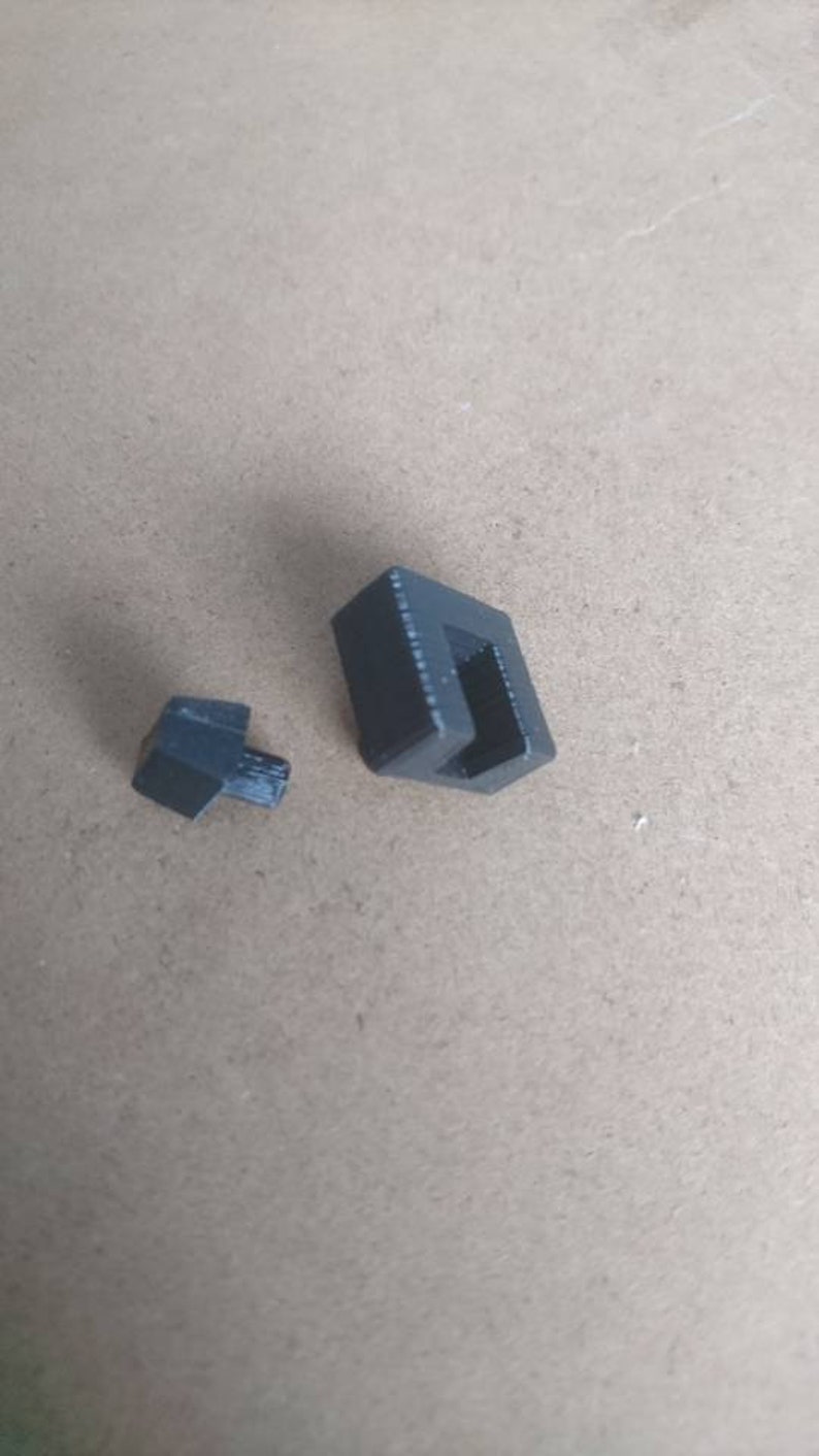 May include: Two black plastic pieces, one is a small square with a hole in the center, the other is a larger rectangular piece with a slot.