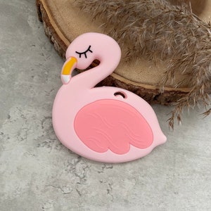 Op de afbeelding: Een roze siliconen baby-bijtje in de vorm van een flamingo met een gele snavel en gesloten ogen.