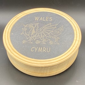 May include: A round wooden box with a black slate top. The slate top features a gold dragon design and the words "WALES" and "CYMRU".
